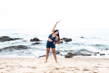 Beautiful young woman in gym clothes doing stretches on the beach sand.