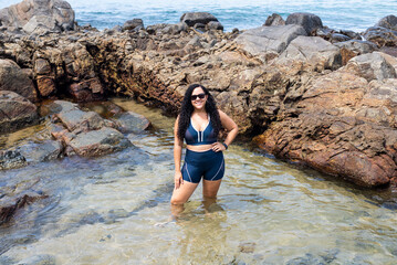 Beautiful, curly-haired woman wearing sunglasses standing in a puddle of water on the beach.