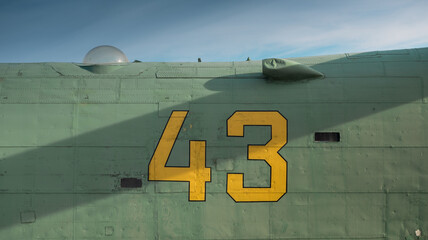 Number 43 written on side of old green aircraft. Metal surface with rivets partially covered with diagonal shadow
