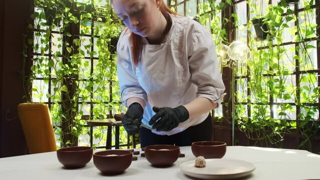 Woman confectioner changes position of candy on plate. Woman chef finishes first candy to present students during cooking lesson