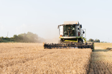 Young farmer driving combine harvester with header on dry wheat field