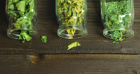 Dry aromatic herbs in glass jars. Wooden table, top view.
