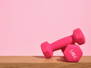 Healthy lifestyle. Pink sport dumbbells on a wooden table. Copy space for text.