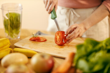 Cropped picture of hands cutting tomato in kitchen.