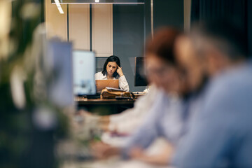 A CEO is sitting at her office and working while worker sitting in a blurry foreground.