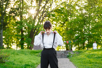 A beautiful girl in a white shirt, in black trousers with suspenders against the background of the...