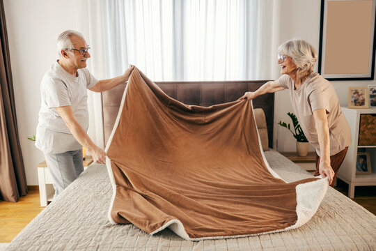Morning routine of senior couple. They are making bed in bedroom together. - Powered by Adobe