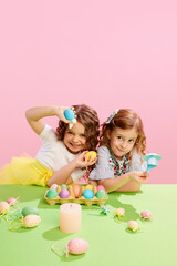 Obraz na płótnie Canvas Beautiful little girls holding painted, decorated Easter eggs against pink background. Happiness. Concept of Easter holiday, celebration, traditions, childhood, happiness