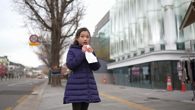 冬の寒い日に韓国のソウルで韓国人の女の子が揚げパンを買って食べているスローモーション映像  Slow motion video of a Korean girl buying and eating fried bread in Seoul, South Korea on a cold winter day