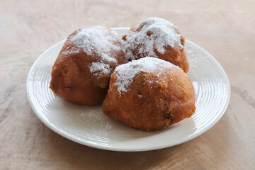 Typical dutch food commonly known as dutch doughnuts, dutchies or oliebollen with currants and powdered sugar on a white plate. Traditionally eaten on new year's eve in the Netherlands.