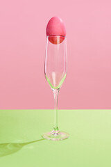 Pink painted egg on champagne glass against pink background. Concept of Easter holiday, celebration, traditions, happiness. Postcard. Empty space for ad