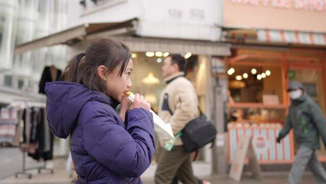 冬の寒い日に韓国のソウルで韓国人の女の子が揚げパンを買って食べているスローモーション映像  Slow motion video of a Korean girl buying and eating fried bread in Seoul, South Korea on a cold winter day