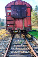 Front view of a rusty red metal freight car on disused train tracks at old station, coupling stops,...
