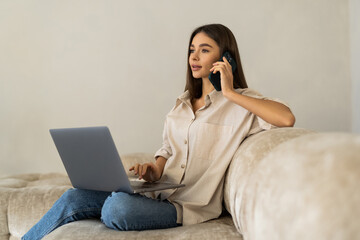 young woman using laptop and phone on sofa at home