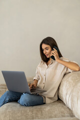 young woman using laptop and phone on sofa at home