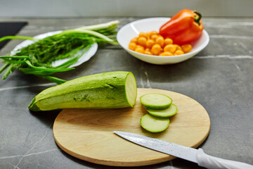 Close up photo of woman's hands holding fresh salad while standing at kitchen table full of fresh vegetables for salad bowl
