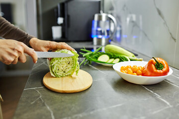 Close up photo of woman's hands holding fresh salad while standing at kitchen table full of fresh vegetables for salad bowl