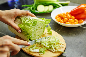 Close up photo of woman's hands holding fresh salad while standing at kitchen table full of fresh...