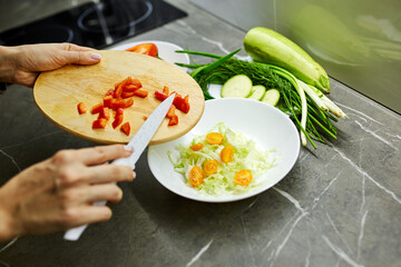 Close up photo of woman's hands holding fresh salad while standing at kitchen table full of fresh vegetables for salad bowl