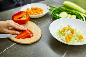 Close up photo of woman's hands holding fresh salad while standing at kitchen table full of fresh vegetables for salad bowl