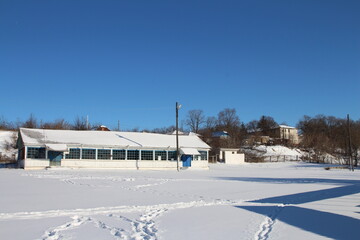 A snowy field with a building and trees in the background
