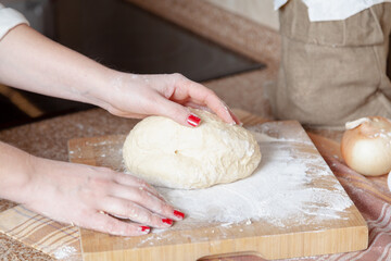 Women hands lie on piece of dough and a board....