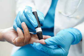 Asian doctor using lancet pen on senior patient finger for check sample blood sugar level to...