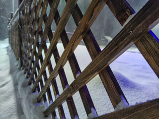 Wooden fence with rhombus planks and snowflakes on a winter evening with a snow storm. Background,...