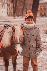 the boy stands next to the pony and hugs the pony's neck looking forward