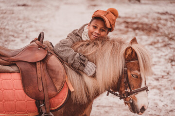 boy hugs pony by the neck looking at the camera from behind the mane