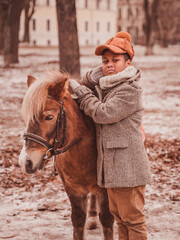 the boy leans his elbow on the pony and looks displeasedly to the side