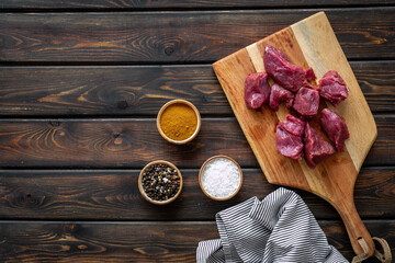 Raw beef meat cutting into pieces on wooden board with spices