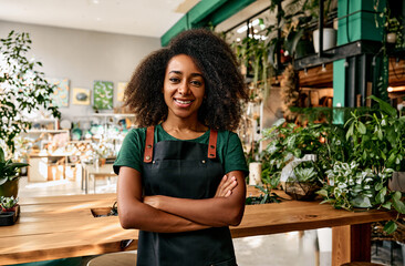 Beautiful smiling curly African American woman in green t-shirt and apron standing with arms...
