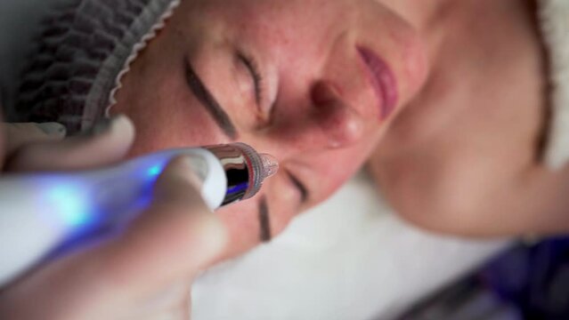 Cosmetologist doing hydrafacial treatment with vacuum machine on woman face in aesthetic beauty clinic