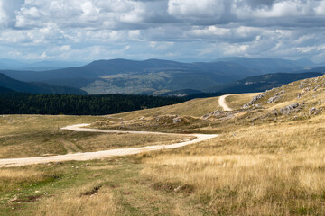 Fototapeta premium Winding road through mountain landscape, distant mountain ih haze and cloudy sky