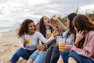 friends having a snack on the beach eating fruit and drinking juice - obrazy, fototapety, plakaty