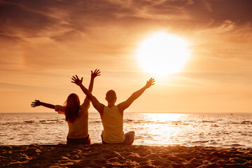 Fototapeta premium Happy young heterosexual couple is sitting with open arms at sunset beach and enjoys the view