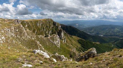 Mountain view from Vlasic near Travnik, rocky slopes overgrown with grass in sunlight and hazy mountains in distance during cloudy day