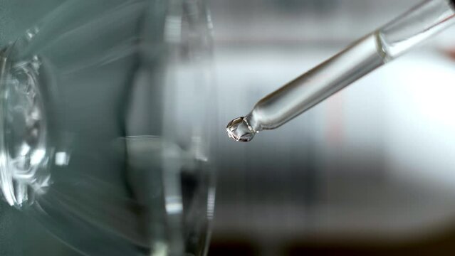 Transparent liquid serum or gel dripping from a pipette into a glass bowl, close-up, macro