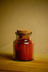on a wooden board aromatic dry red paprika (spices) in a glass jar and a stopper next to it