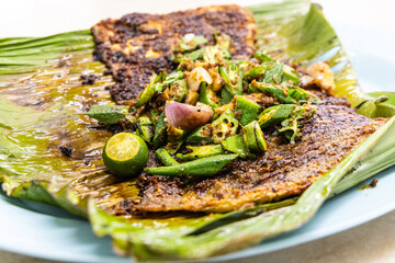 Close-up of grilled stingray fish with spices topped with okra vegetable on banana leaf popular food in Malaysia