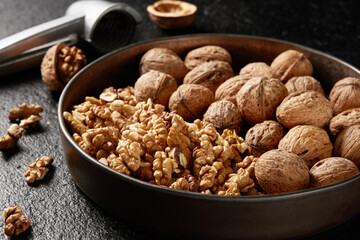Close-up of a bowl of shelled kernels and whole walnuts on a dark background.