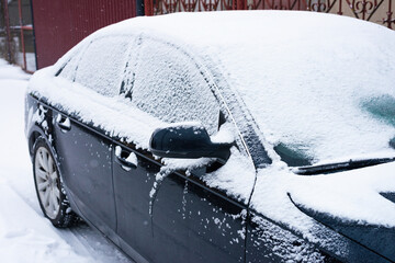 Parked modern dark colored car covered with snow in winter season.