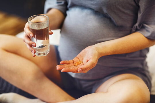 Pregnant woman taking prenatal vitamins during pregnancy, holding water glass and pill in her hands