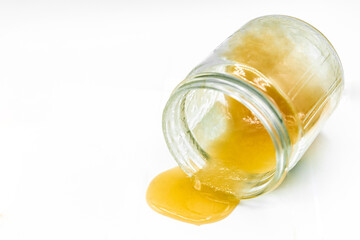 Honey is pouring out of a jar on a white background