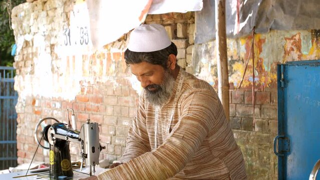 A Muslim tailor sewing clothes and showing thumbs - smiling  salt and pepper  long beard  middle-aged man. A man showing a sign of approval while working at a sewing machine - concept of employment...