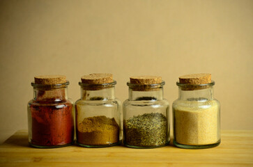 various spices in small transparent jars stand on a wooden board