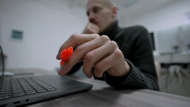 The man thoughtfully twirls a bright orange pen in his hand between his fingers. Unconscious hand gestures during deep thought and concentration. Close-up, wide-angle shot.