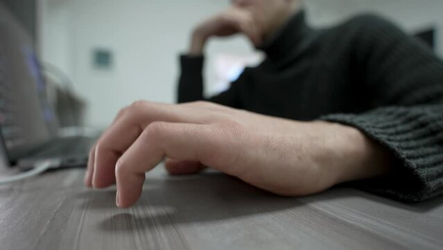 Bored man taps his fingers on table while sitting at his workplace near laptop. Close-up of man hand nervously tapping his fingers on table. Wide angle view male hand with gesture beat to music.