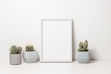 Picture frame mockup with cactus plants in ceramic pots on the white wooden table. Wooden white photo frame with copy space for design, scandinavian cozy home interior - obrazy, fototapety, plakaty